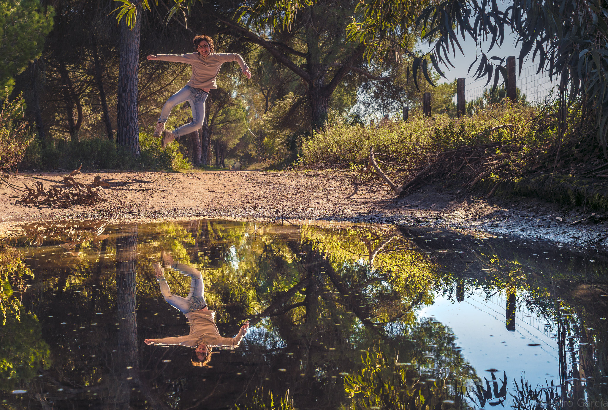 A person leaping in the air jumping into a pool of water, their joyful reflection below on the waters surface