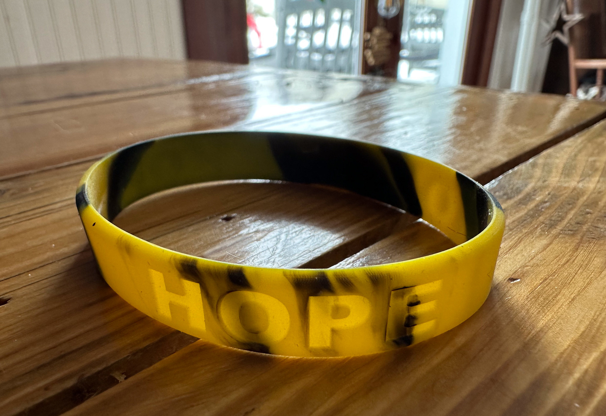 Multicolored rubber wrist band with engraved letters Hope sitting on a wood table, light from a window behind streams onto the table