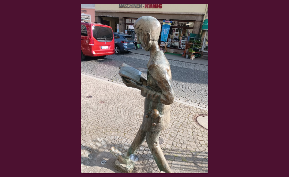 Statue of a man walking down the street reading a book